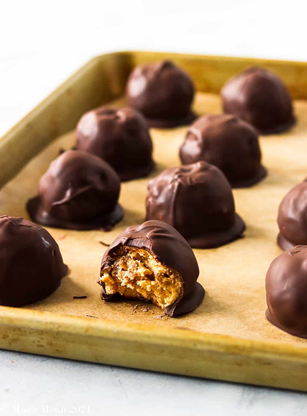 A side shot of a peanut butter bon bon with a bite taken out of it on a baking sheet with other bon bons