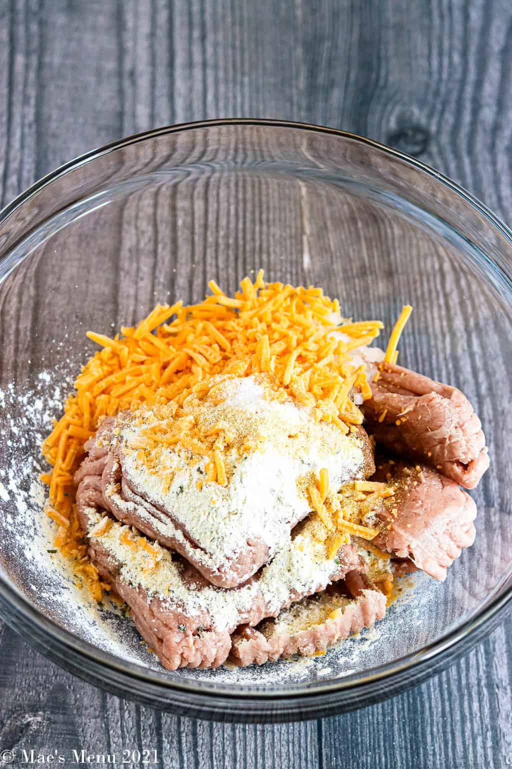An up-close shot of a mixing bowl of ground turkey with ranch dressing mix, seasoning, and shredded sharp cheddar