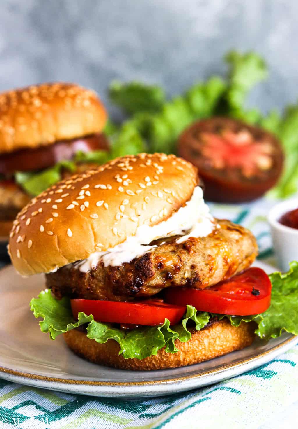 An up-close side shot of an air fryer turkey burger on a plate with another burger on the background