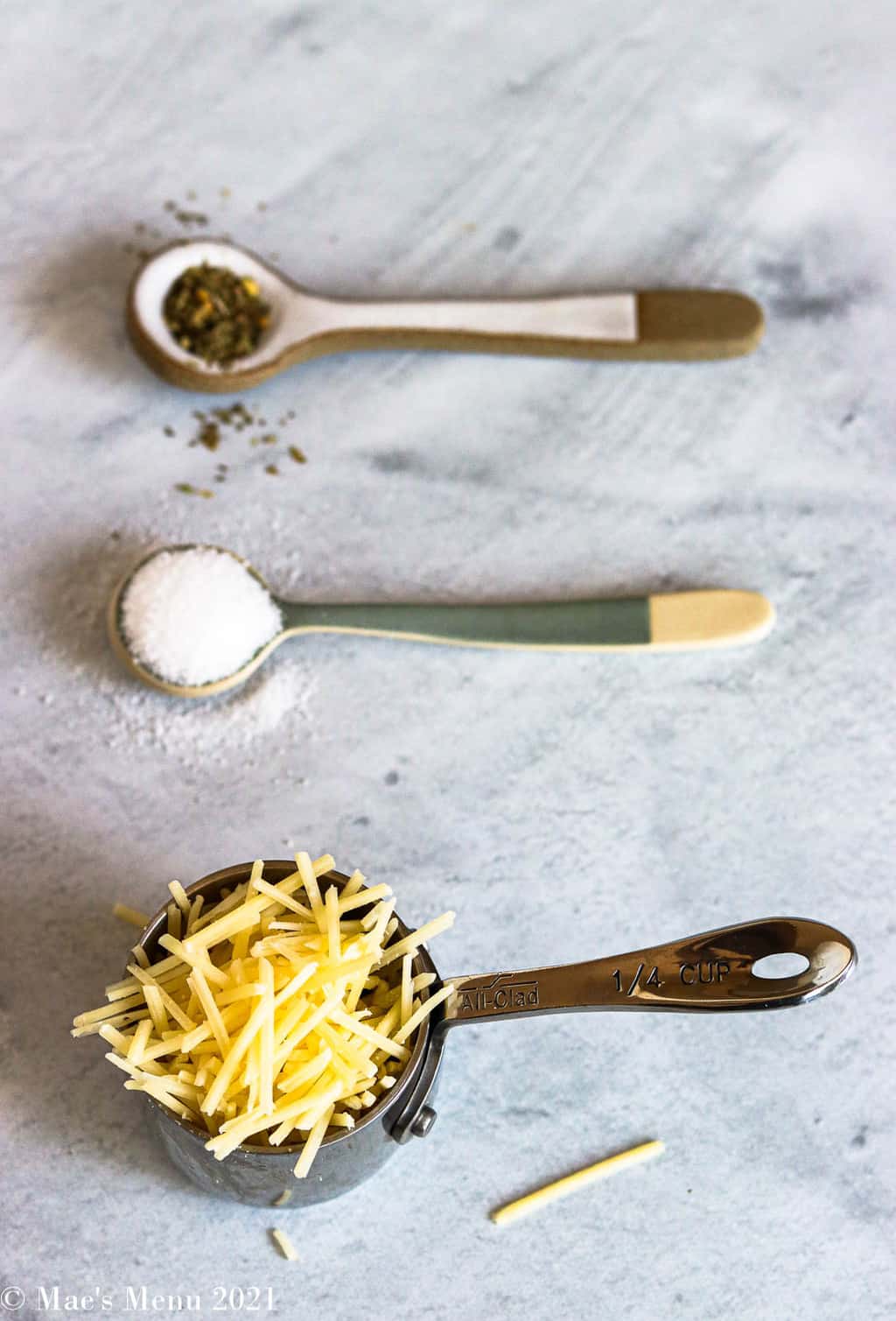 Two small spoons of salt and spices next to a small measuring cup of grated parmesan cheese