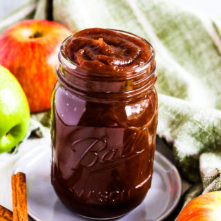 A side shot of a ball jar of instant pot apple butter with a towel and apples in the background