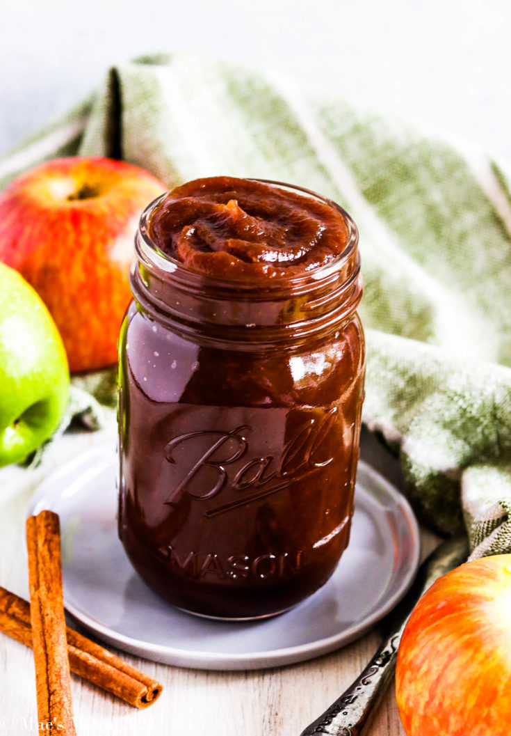 A side shot of a ball jar of instant pot apple butter with a towel and apples in the background