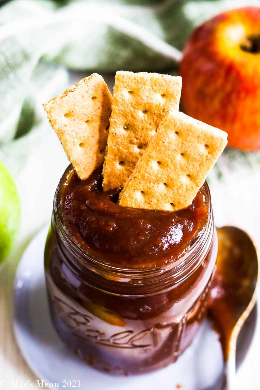 Graham crackers in a jar of apple butter with apples in the background