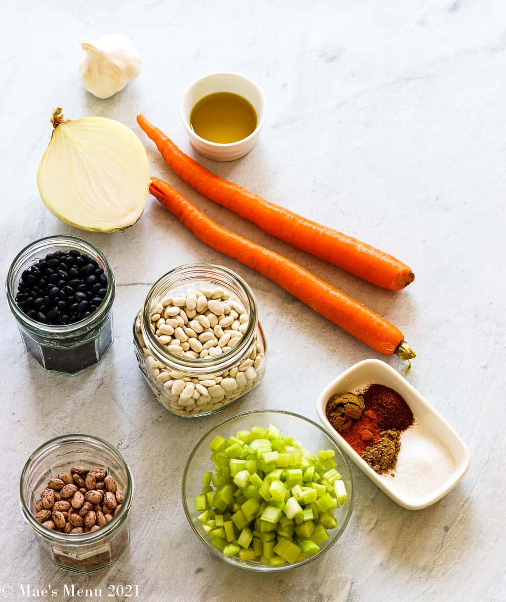 All of the ingredients for instant pot bean soup: dried beans, celery, onions, garlic, olive oil, seasonings, and carrots
