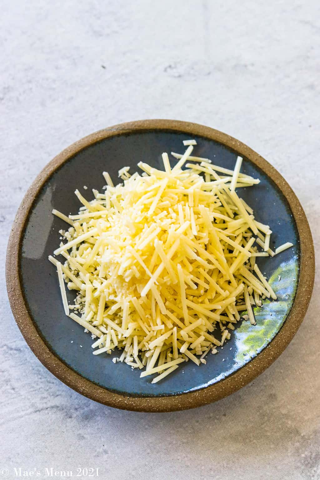 An overhead shot of shredded parmesan cheese on a small blue dish