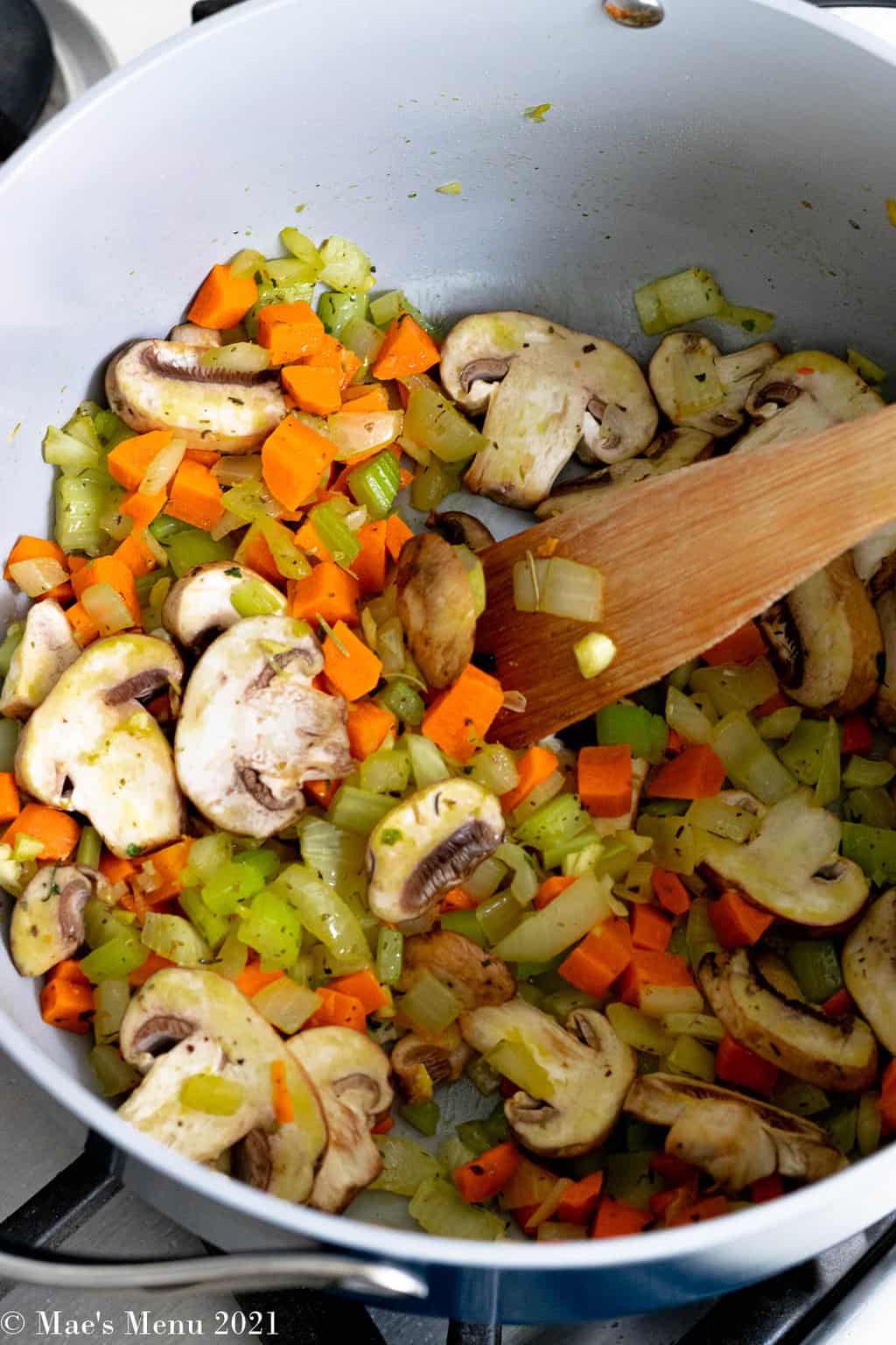 A saute pan of onions, carrots, celery, mushrooms, and herbs