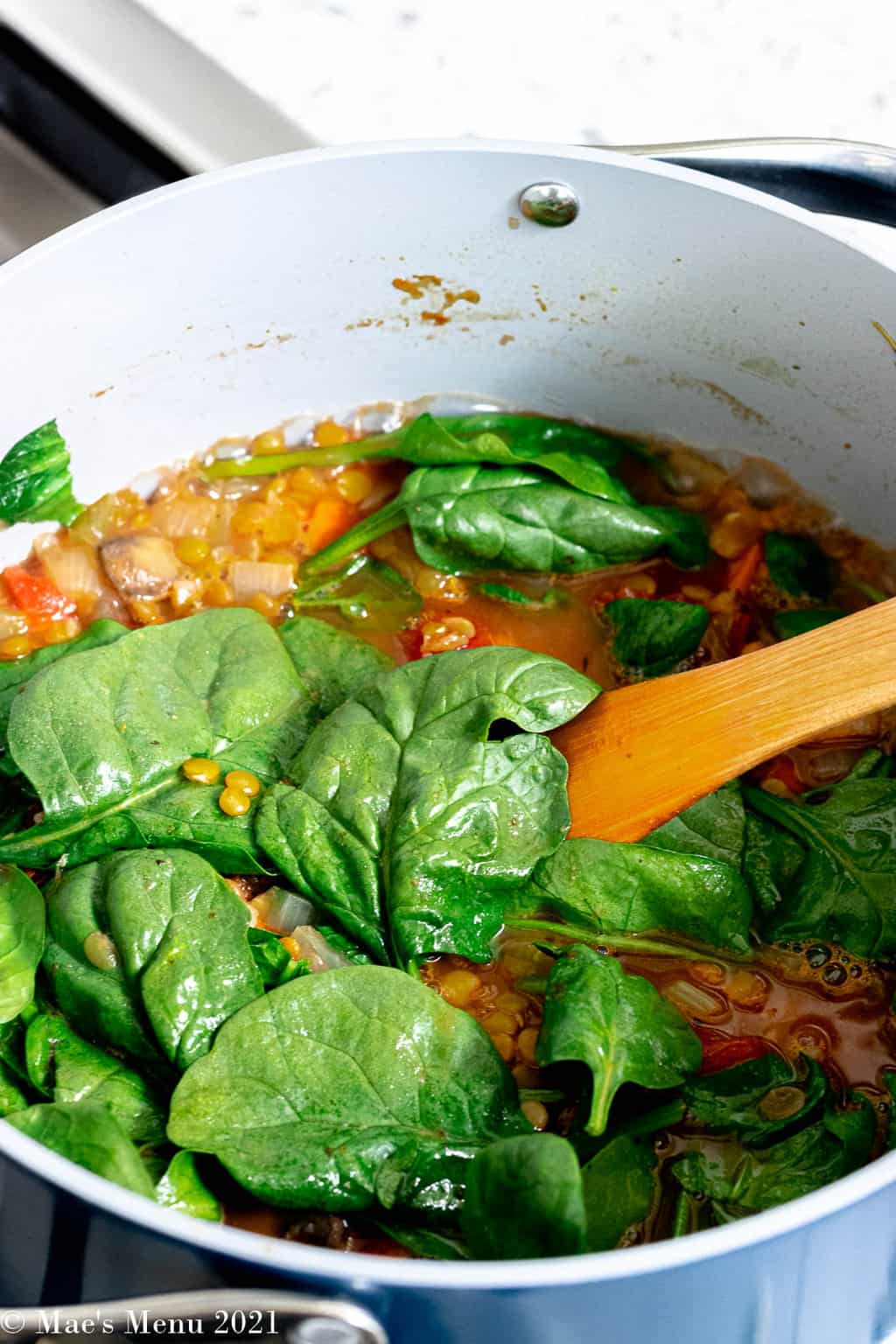 a side shot of a dutch oven of italian lentil soup with fresh spinach added