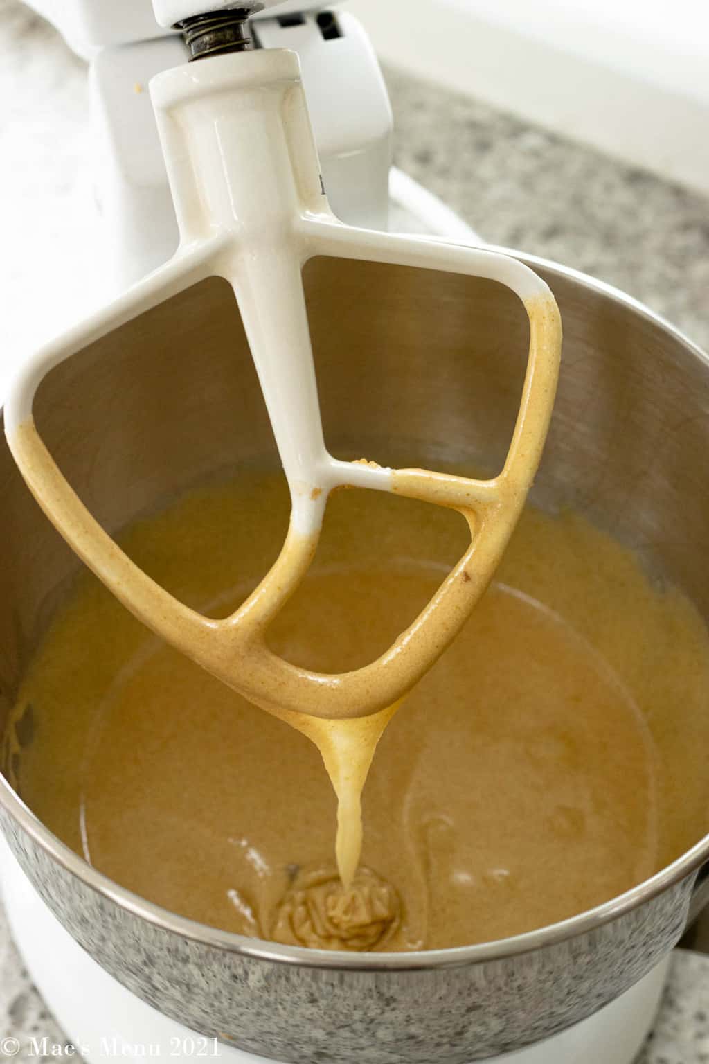 A thick golden batter dripping off the mixing paddle of the stand mixer