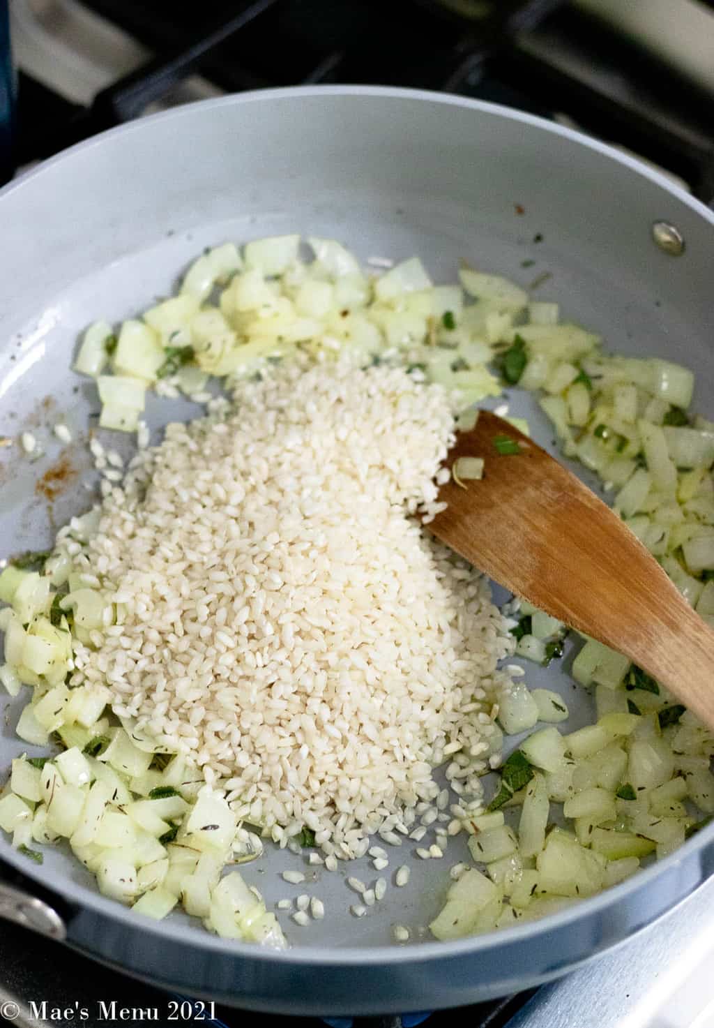 Adding arborio rice to the saute pan with the onions and herbs