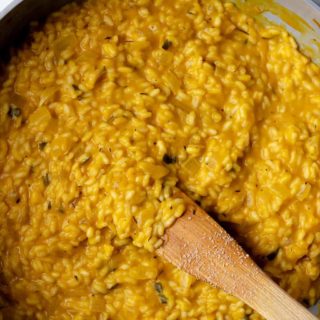 An up-close shot of a pan of pumpkin risotto with a wooden stirring spoon in it