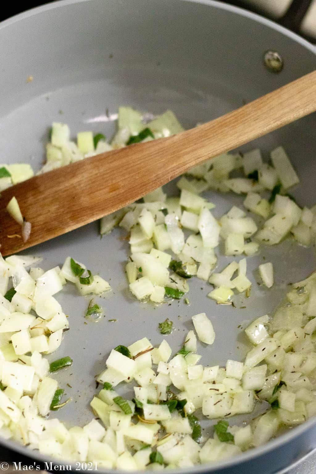 An up-close shot of onions and herbs sauteing in a pan