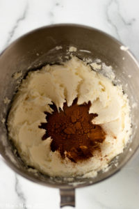 An overhead shot of a mixing bowl with buttercream, cinnamon, and maple syrup