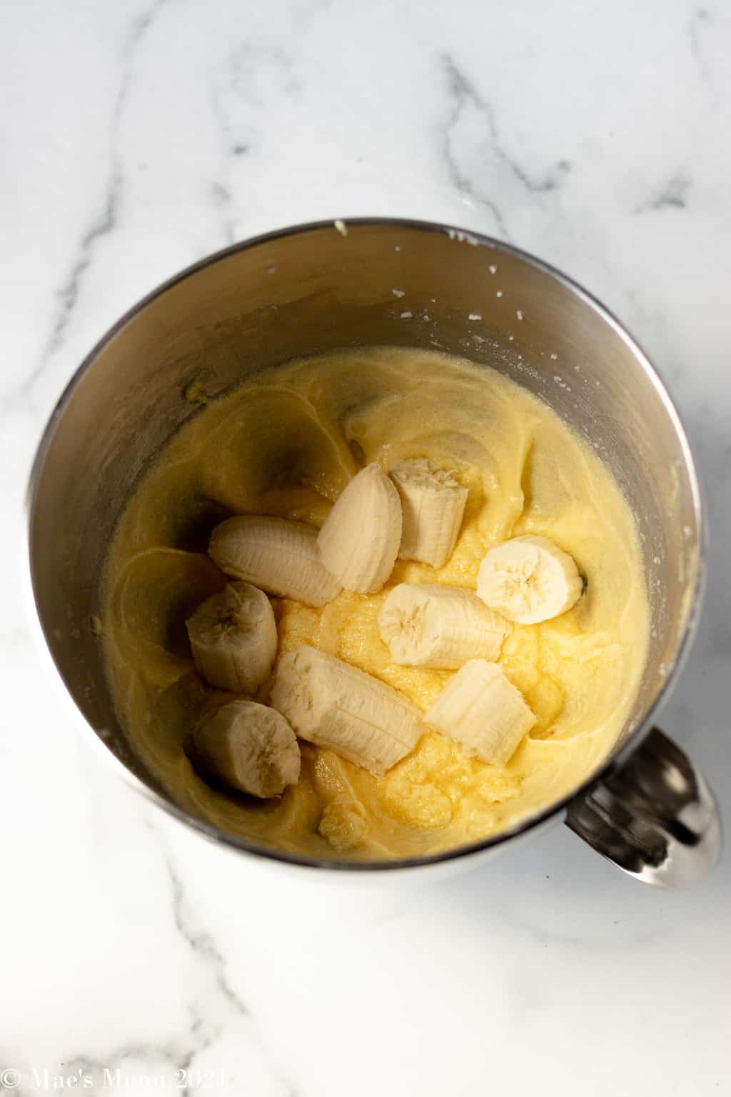 A mixing bowl with creamed butter and sugar and bananas