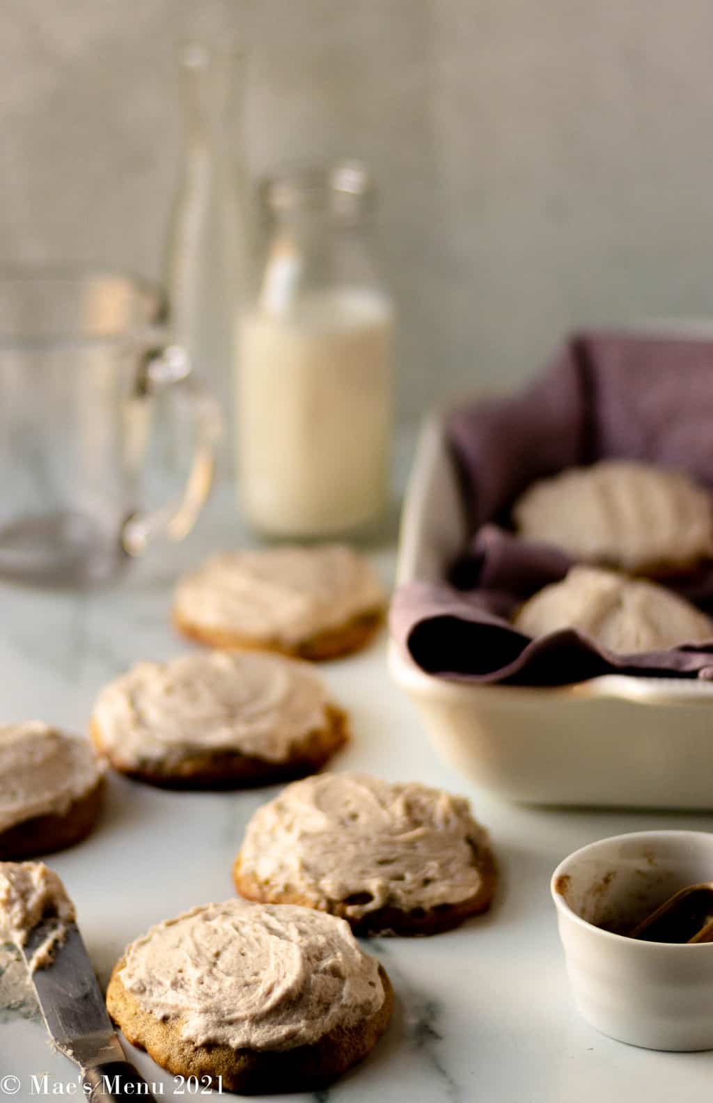 Banana bread cookies on a counter next to a tray of cookies and milk bottles and glasses
