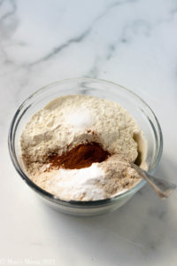 A side shot of a small mixing bowl of flour, cinnamon, salt, and baking soda
