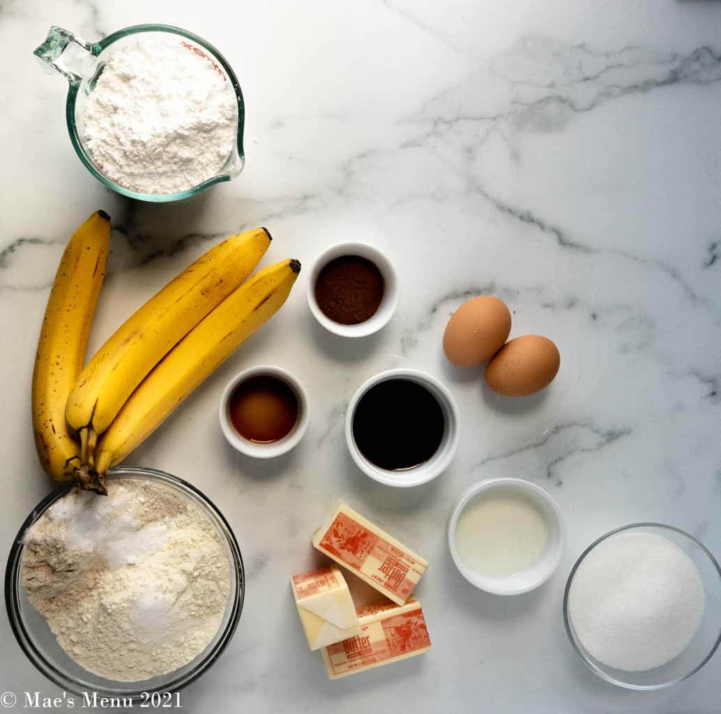 An overhead shot of the ingredients for banana bread cookies: powdered sugar, bananas, flour, baking soda, salt, butter, vanilla extract, cinnamon, maple syrup eggs, milk, sugar