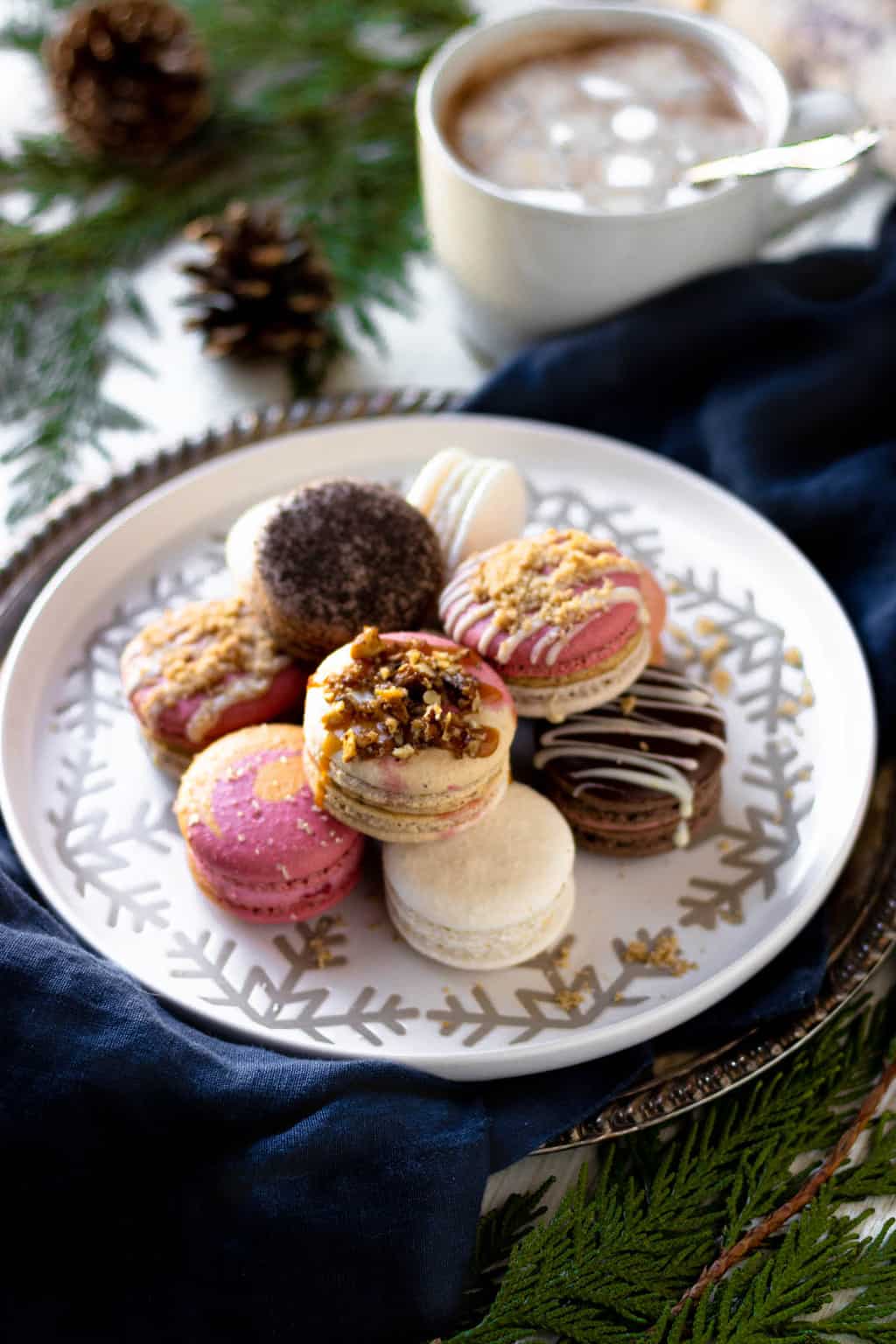 A platter of macarons with hot chocolate and evergreen bows in the background.