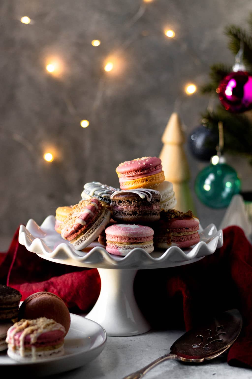 A cake stand of macarons in front of fairy lights and a Christmas tree.