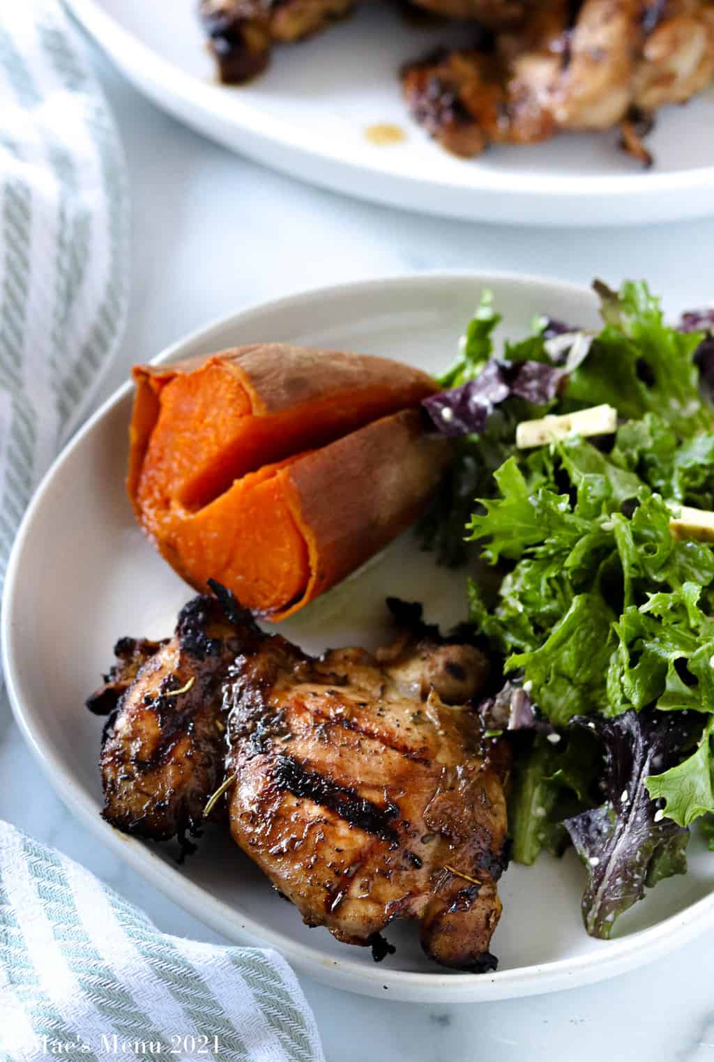 A plate of grilled chicken thighs, sweet potato, and salad