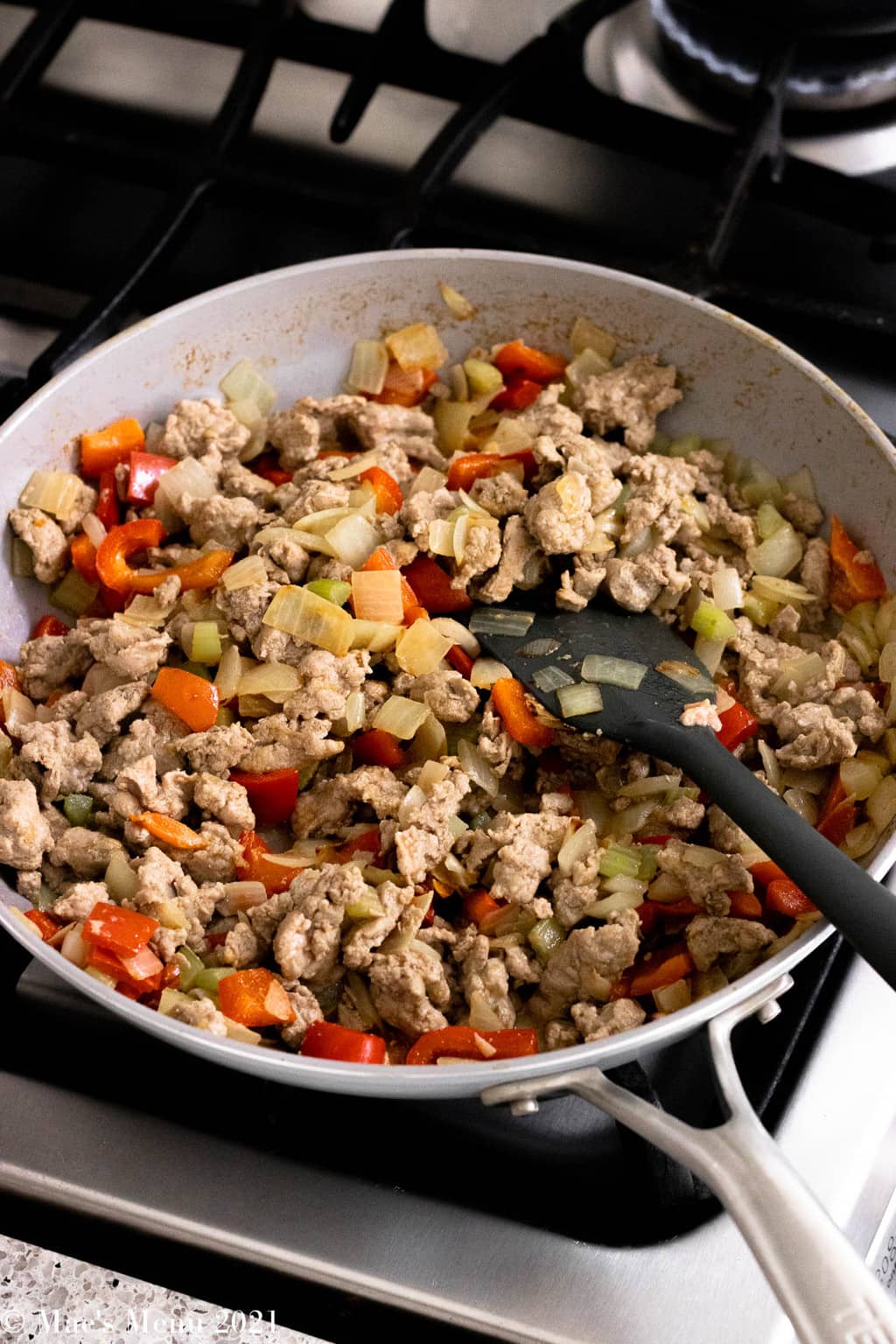 A saute pan of cooked and crumbled ground turkey, onions, celery, and red pepper.