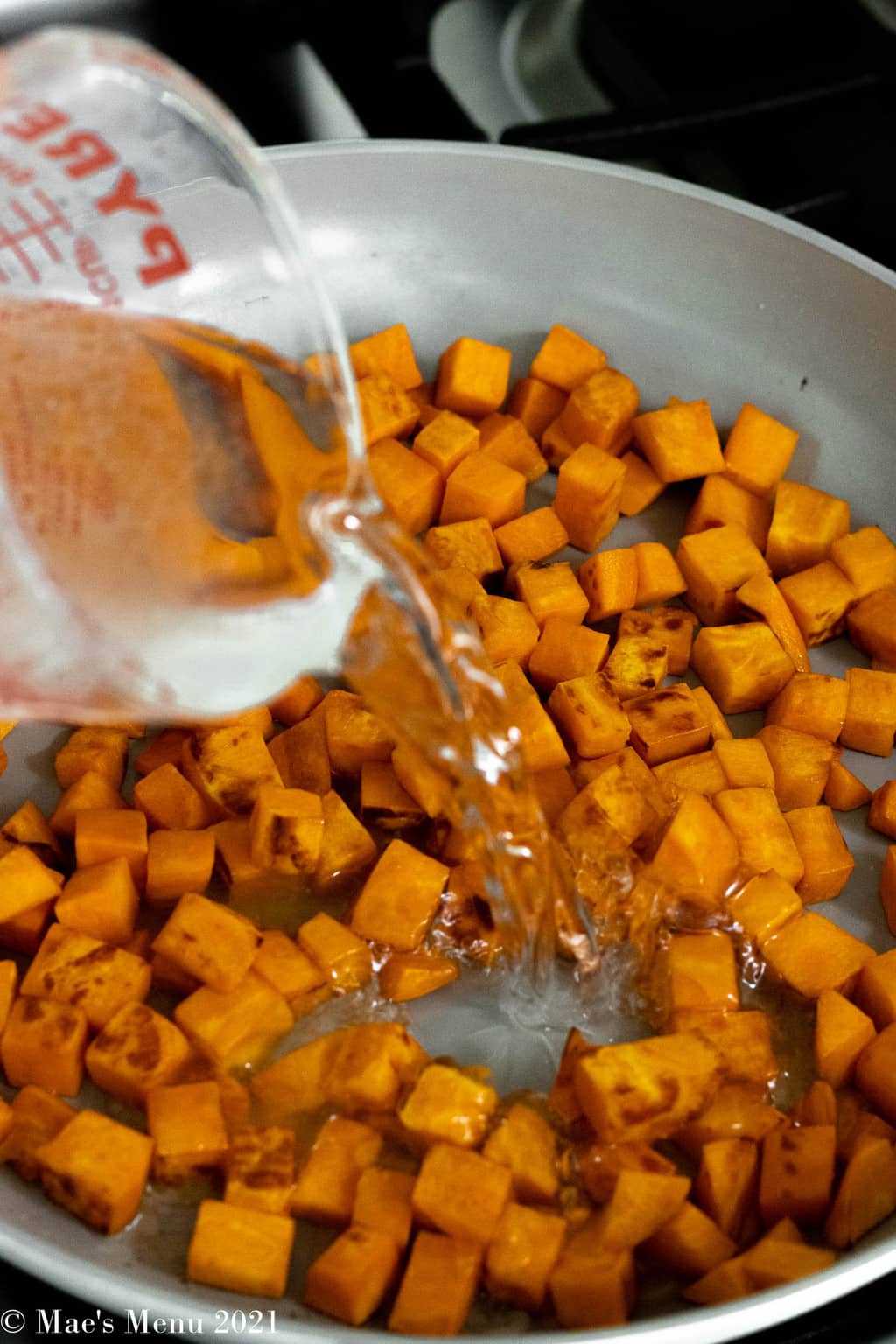 Pouring water in with the pan with the cooking sweet potatoes.