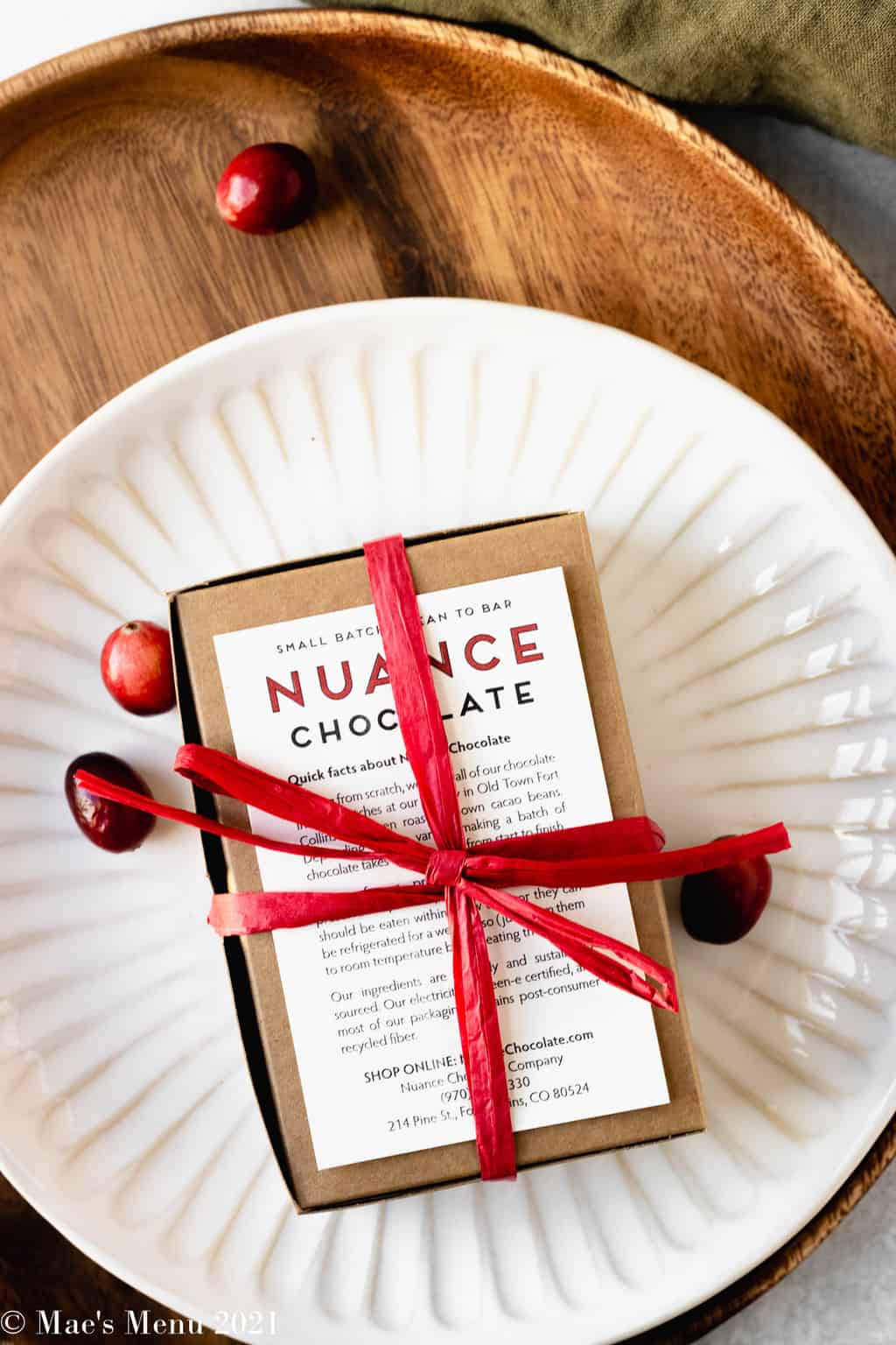 An overhead shot of a box of nuance chocolates wrapped in red ribbon and with sprinkled cranberries around it.