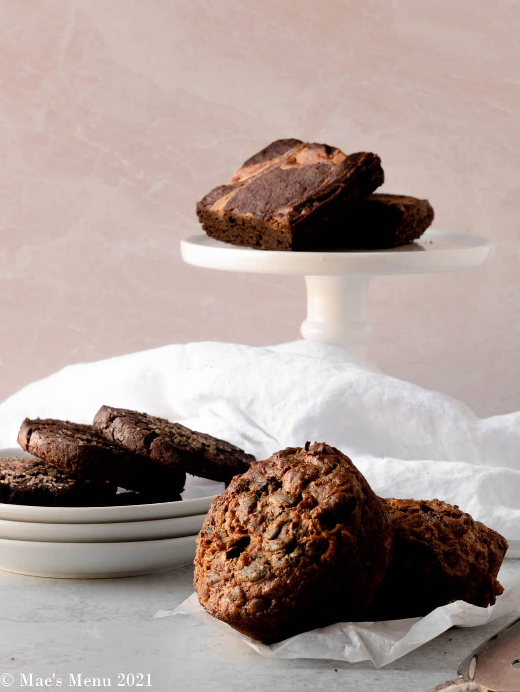 A cake stand of brownies, a dish of chocolate sables, and two muffins in front.