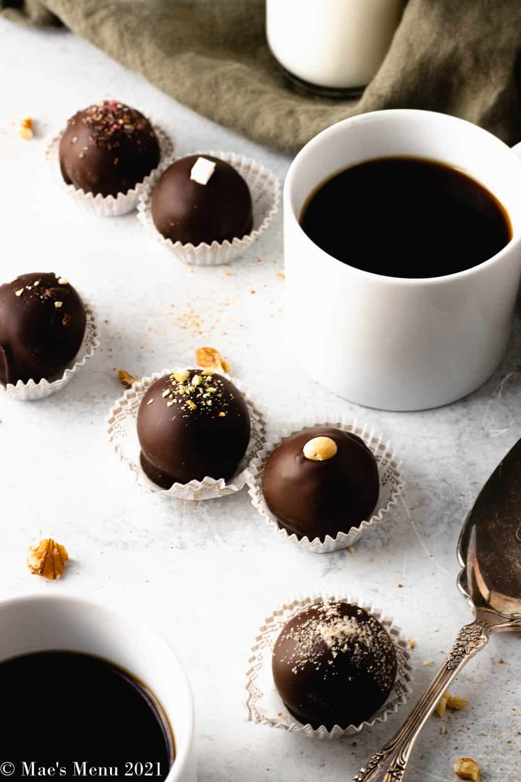 Dark chocolate truffles on a concrete counter with a cup of coffee, serving spoon, and bottle of milk.
