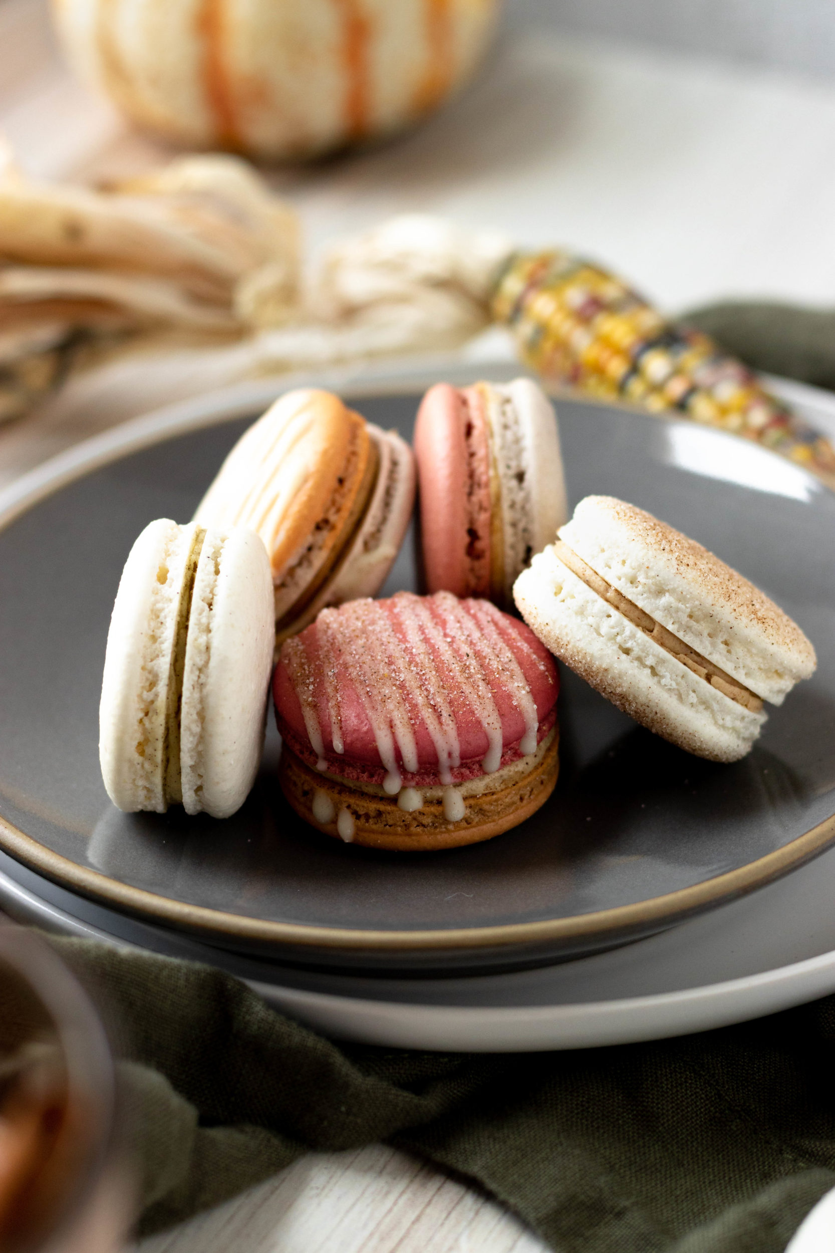 An up-close shot of macarons on a stack of plates surrounded by decorative candy corn and a small pumpkin 
