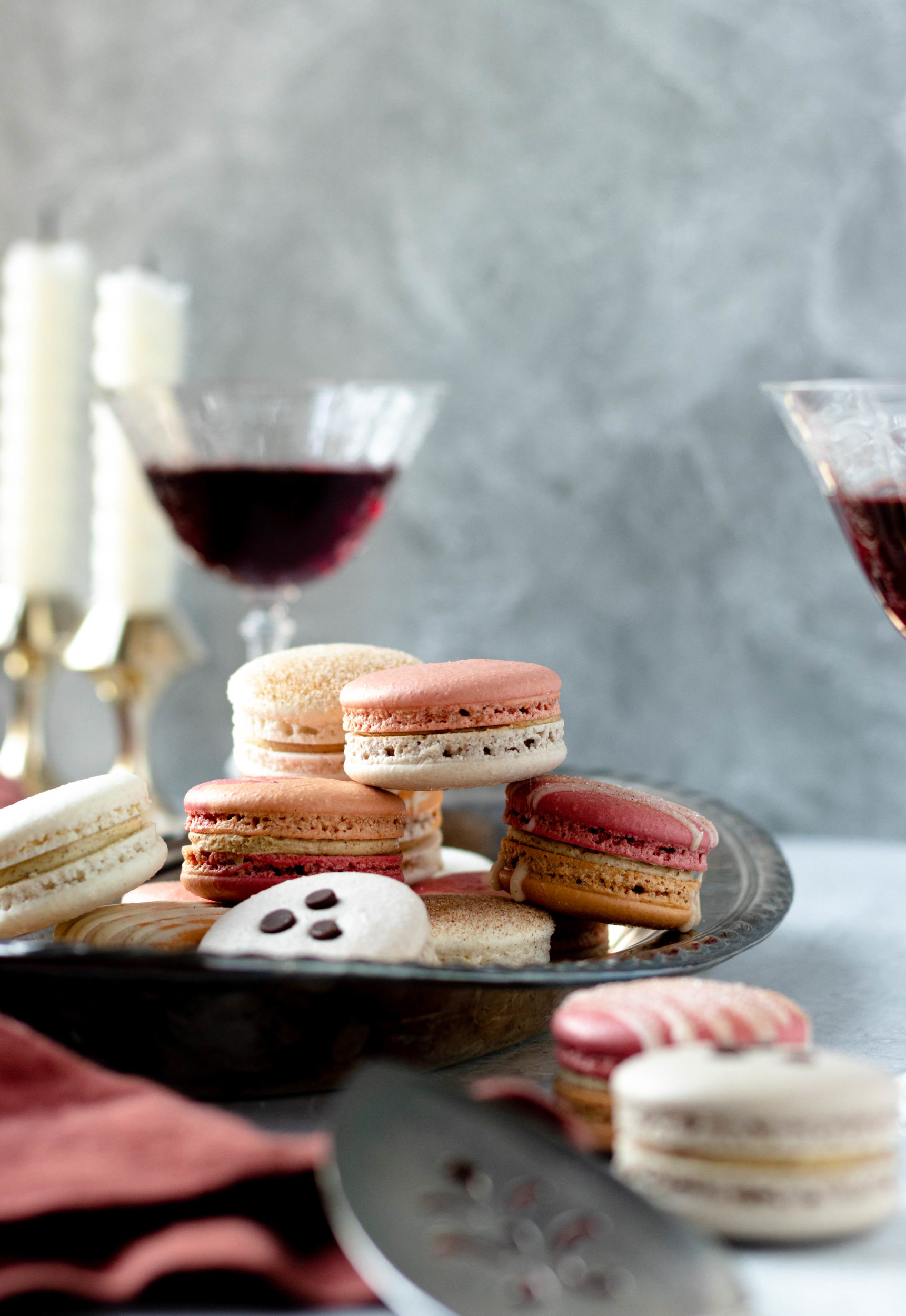 A side shot of a metal tray of macarons surrounded by wine glasses and candles