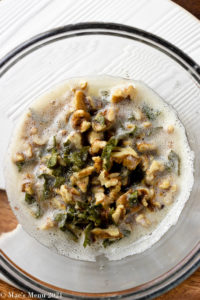 An overhead shot of a glass dish of browned butter with walnuts and sage.