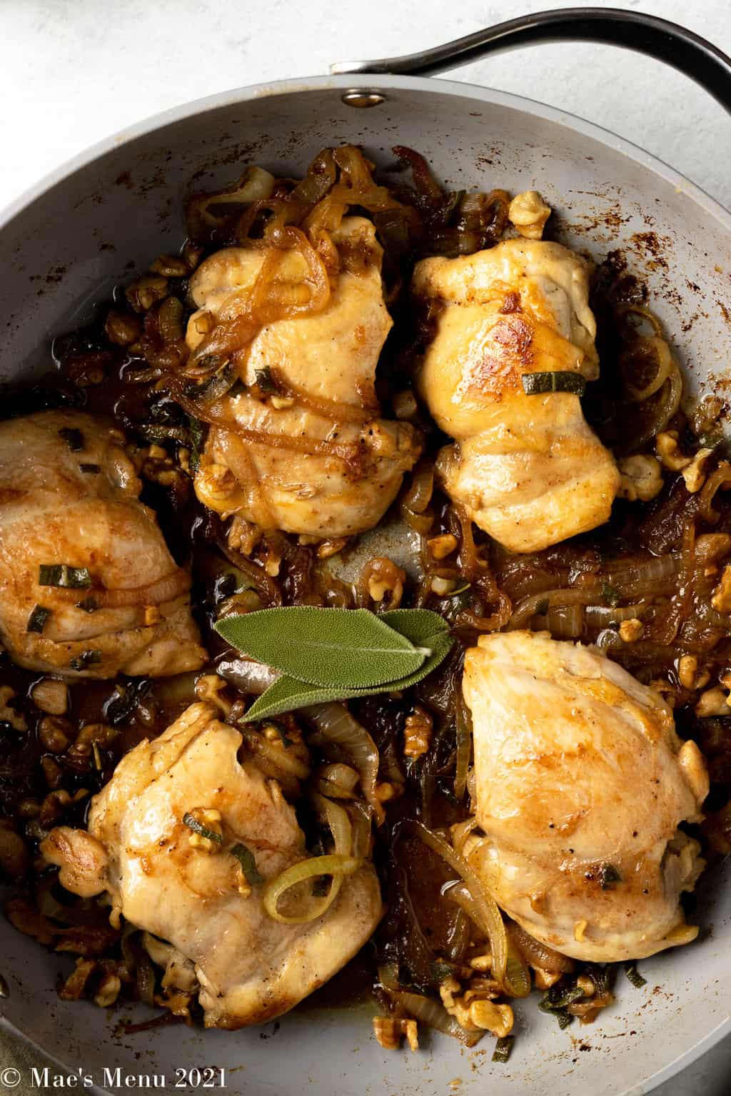 An up-close overhead shot of a pan of sage walnut chicken with brown butter sauce. the dish has two pieces of sage on top.