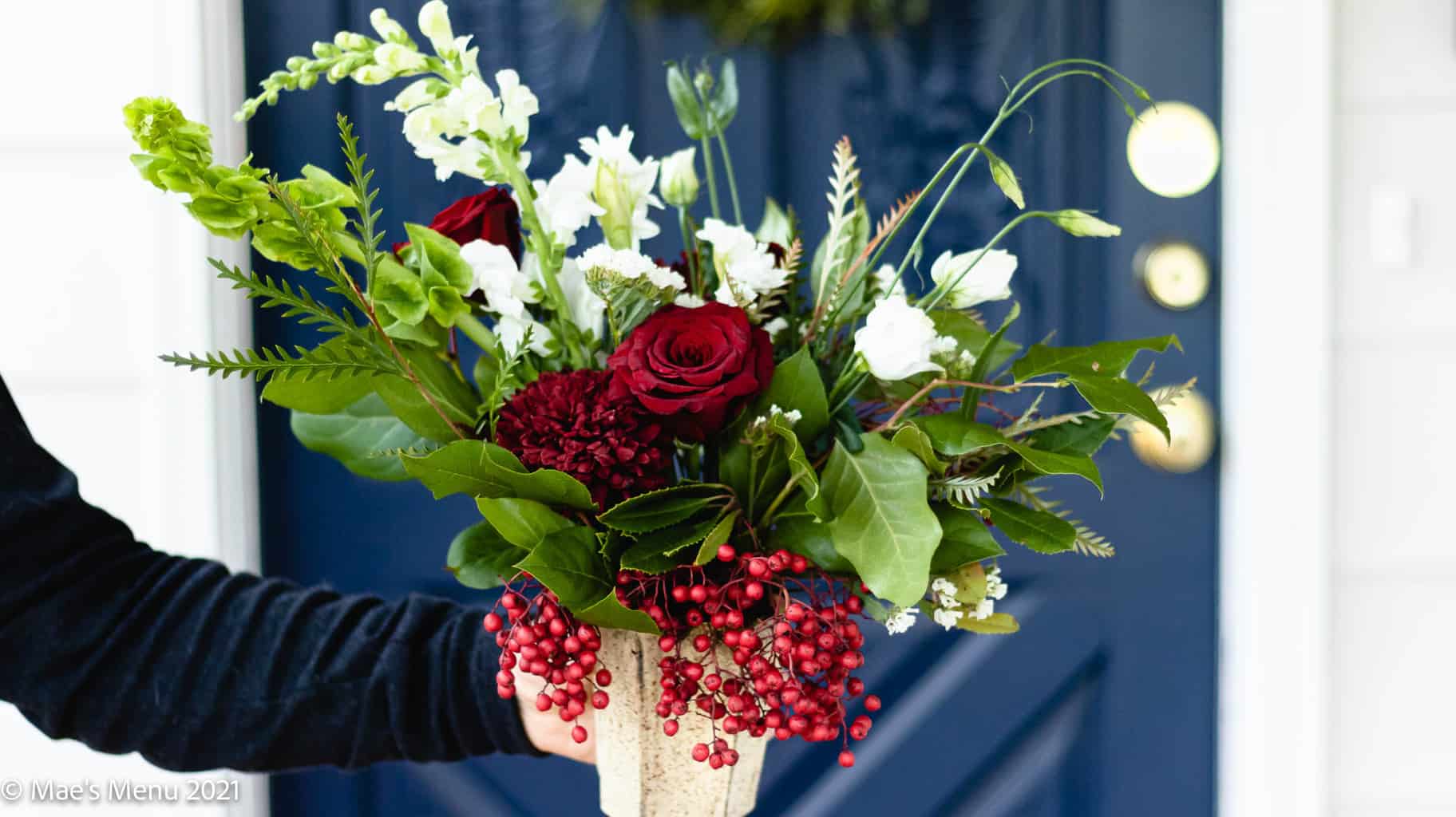 A hand holding a bouquet of Christmas flowers in front of a blue door.