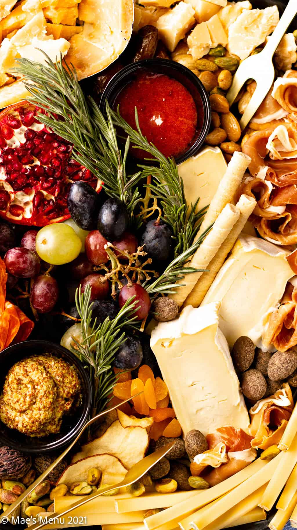 An overhead shot of a charcuterie board with herbs, dried fruit, and nuts.