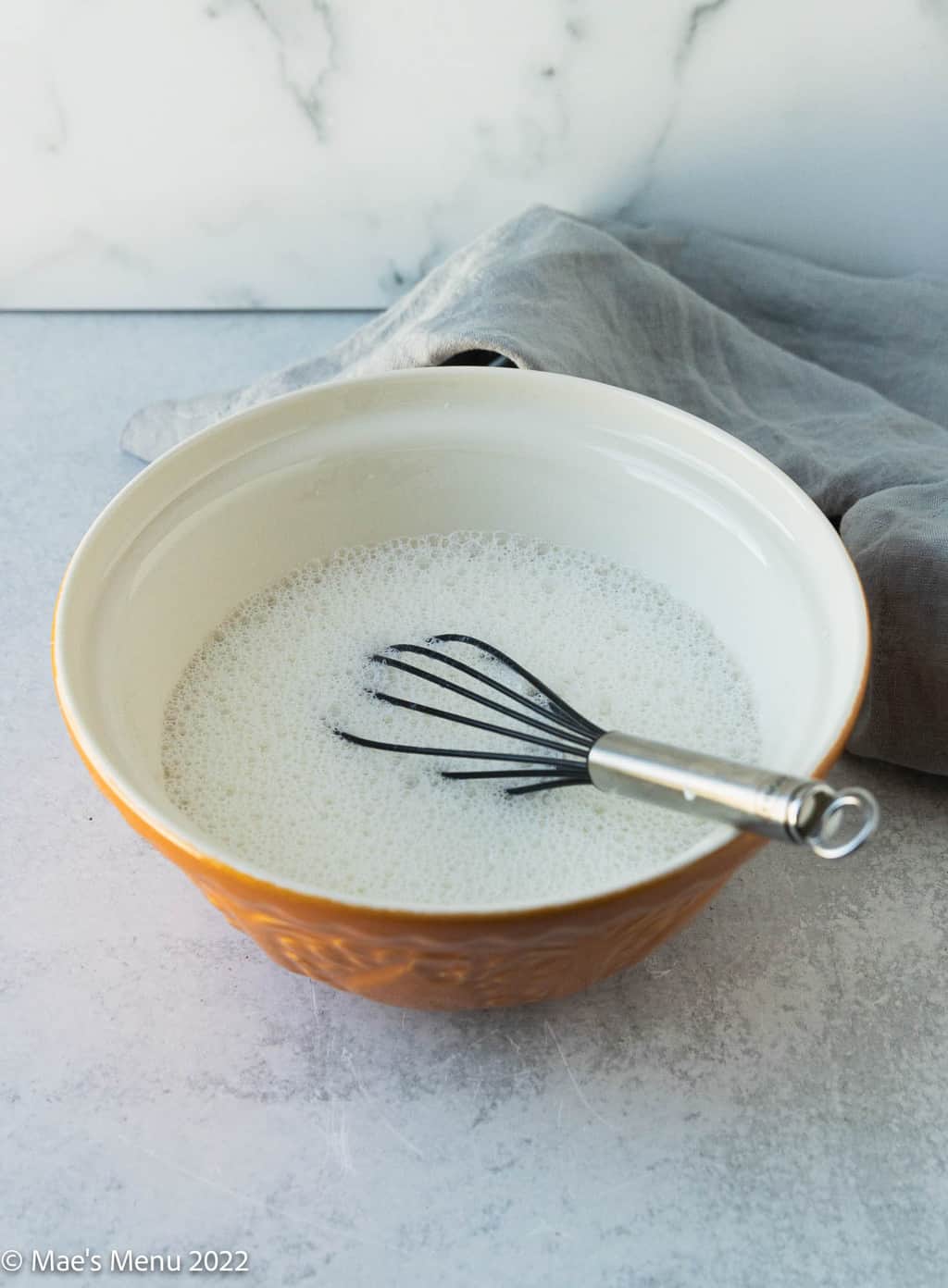 A side shot of a mixing bowl of frothy milk and a whisk.