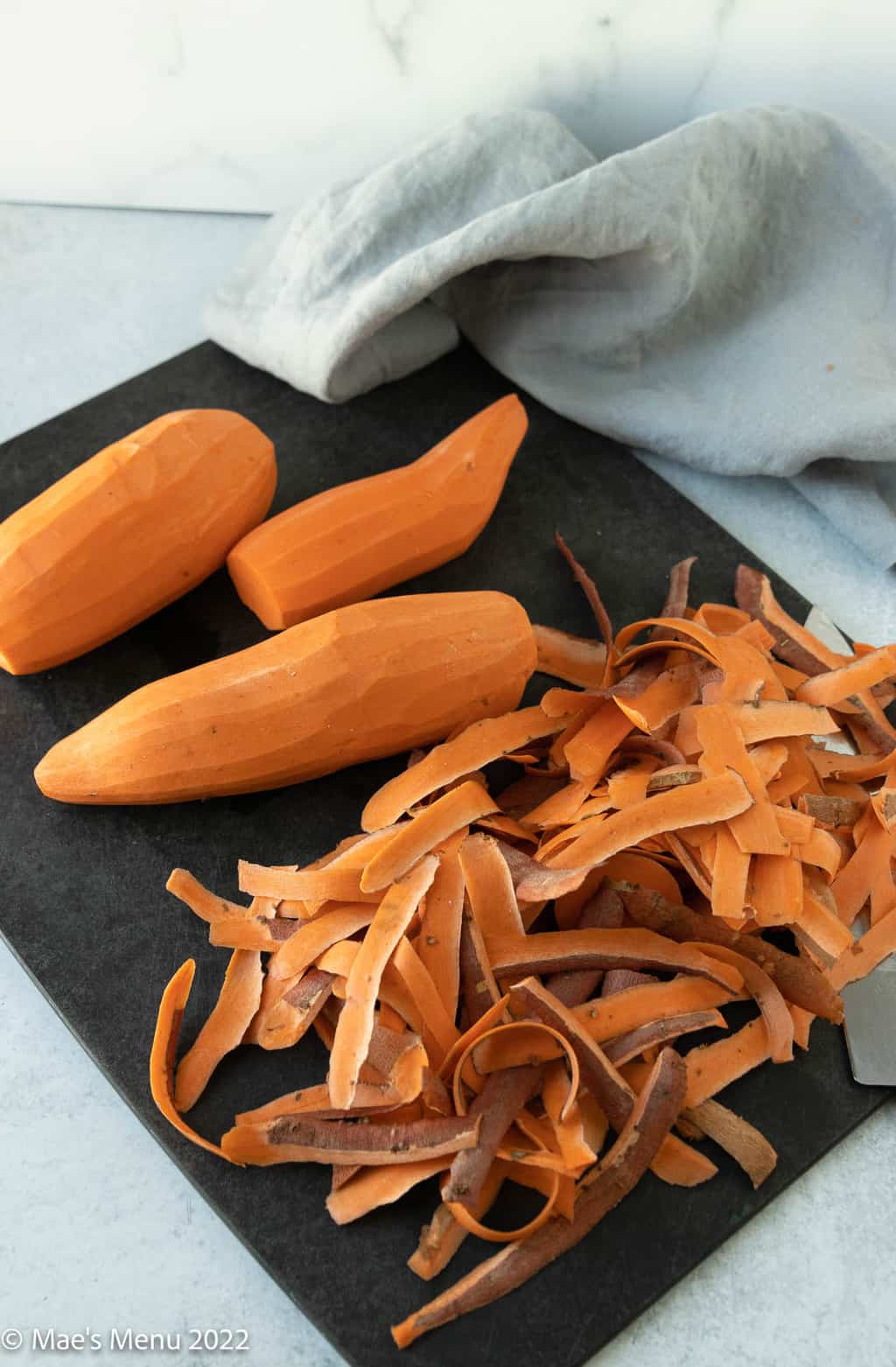 A cutting board with peeled sweet potatoes.