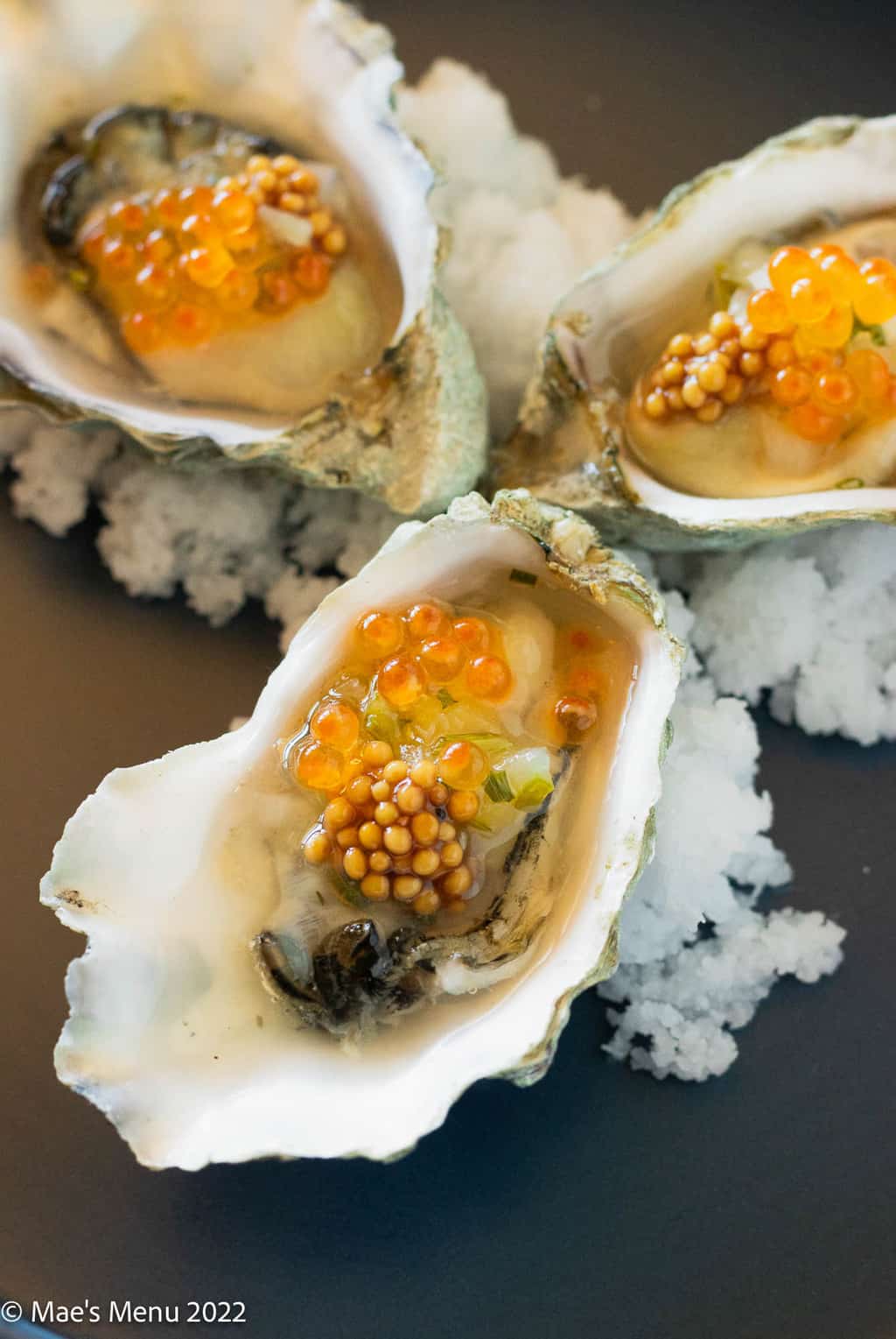 An up-close shot of 3 oysters with caviar and mustard seed.