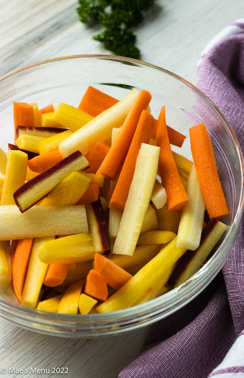 An elevated side shot of a clear bowl of cut up rainbow carrots.