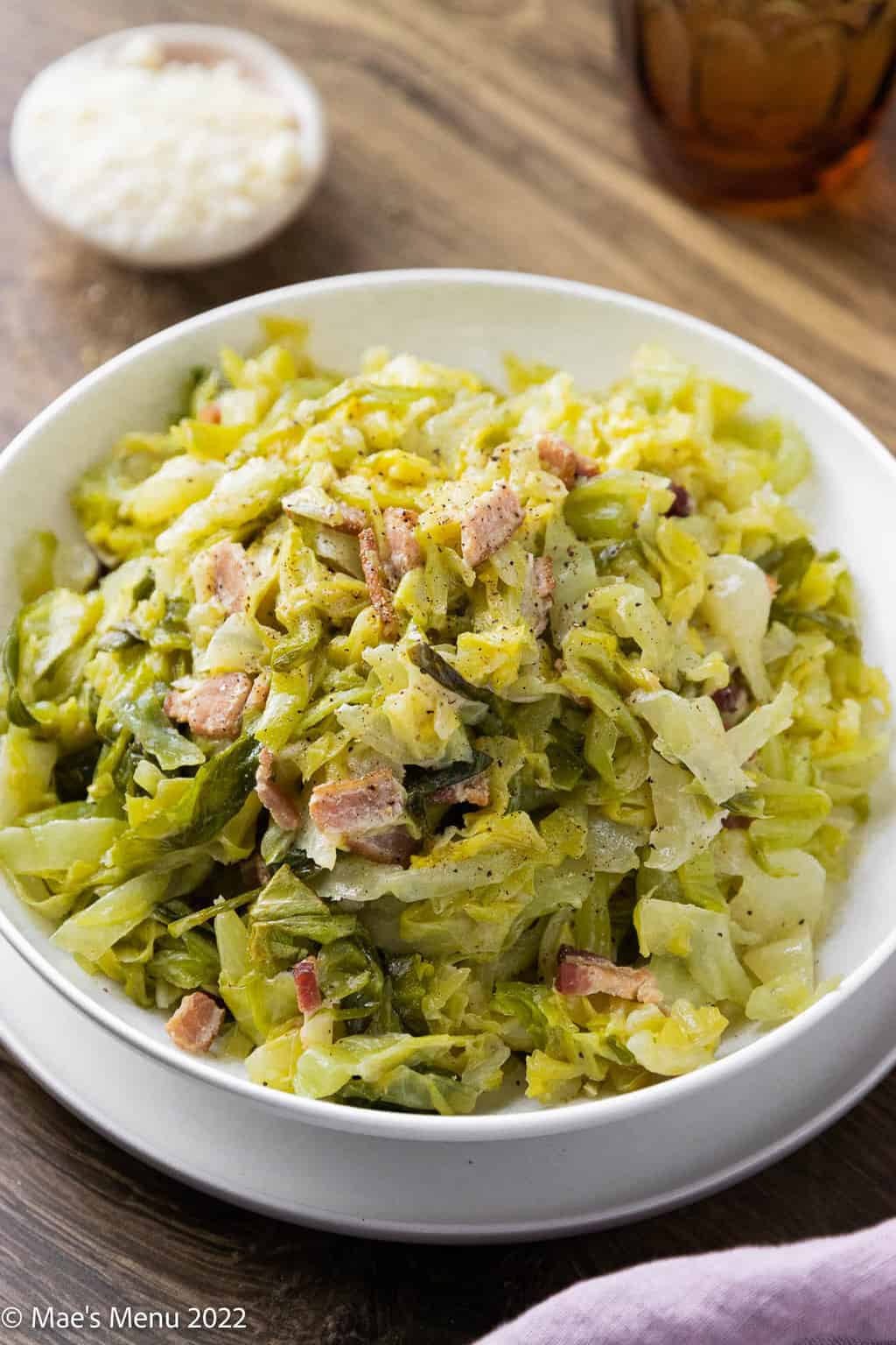 An angled shot of a white bowl of creamy braised cabbage with bacon.