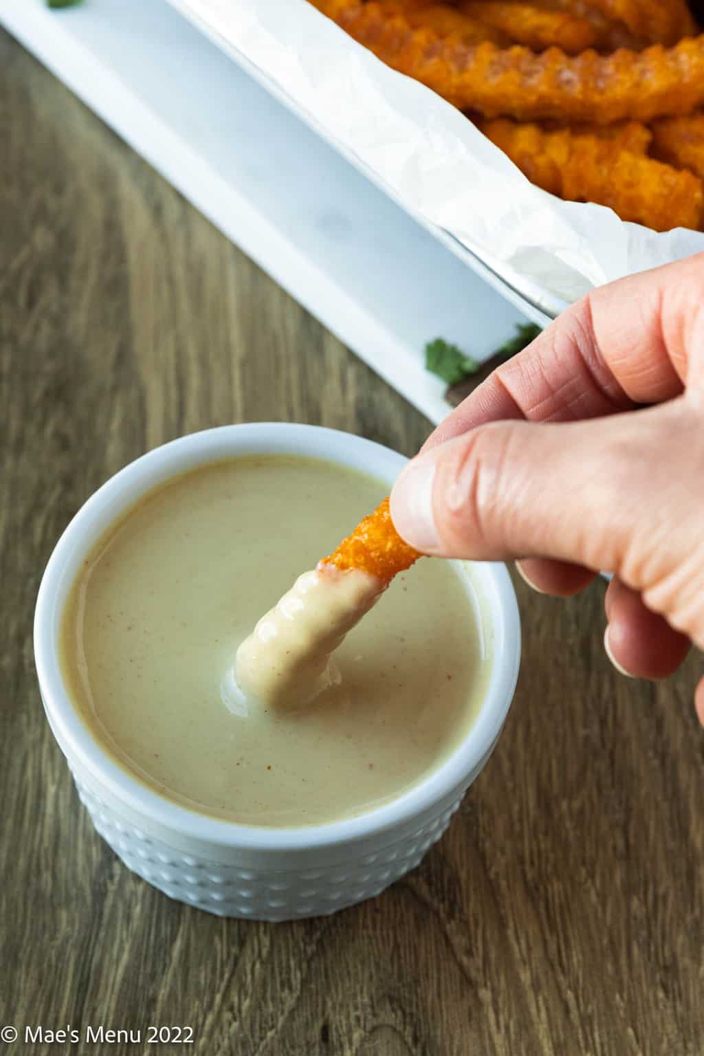 A hand dipping a sweet potato fry into a small cup of honey mustard dip.