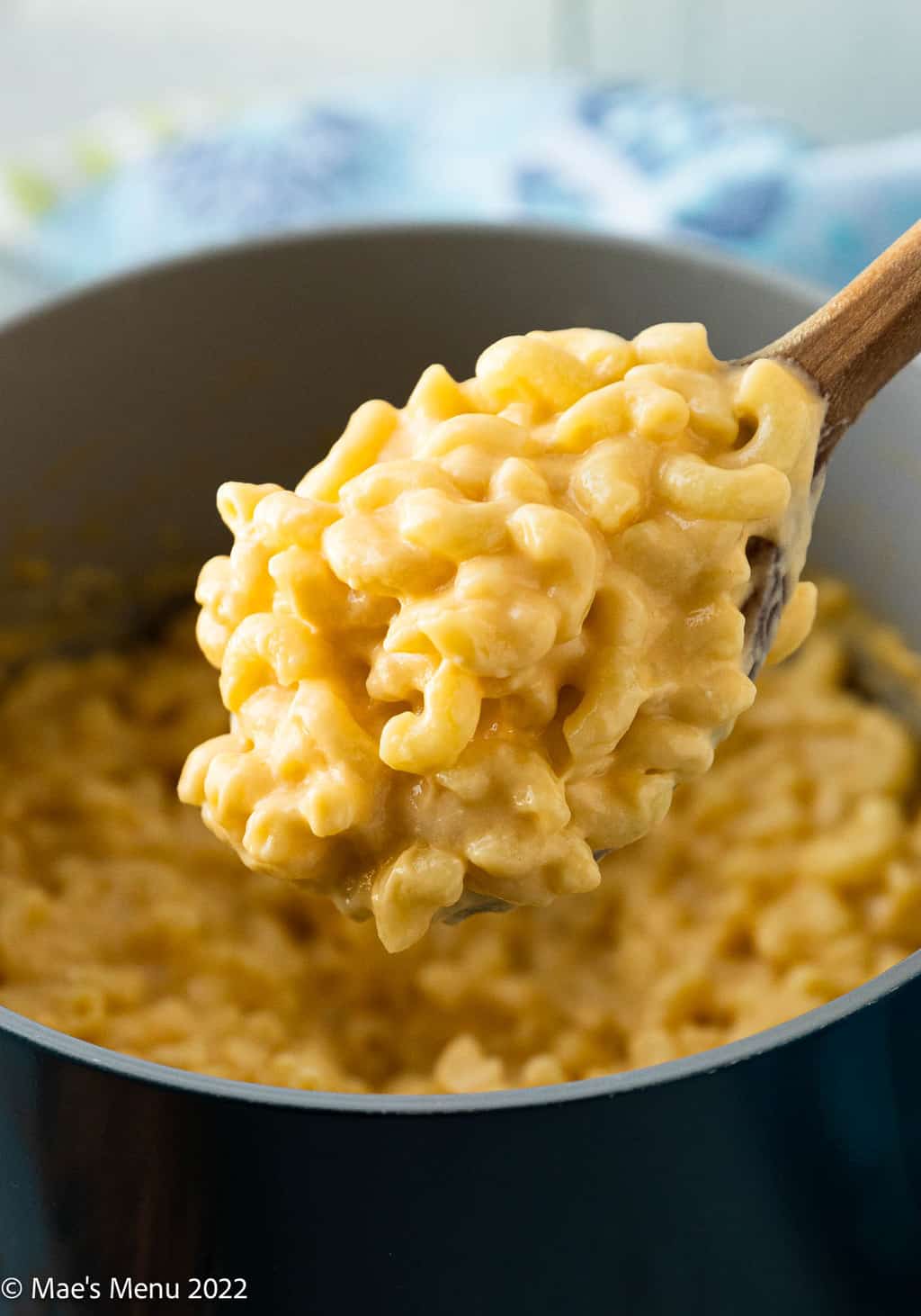 An up-close shot of a wooden spoonful of Greek yogurt Mac and cheese in front of the pan of mac and cheese.