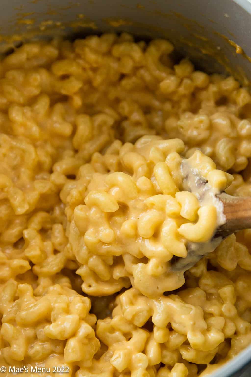 An up-close shot of a wooden spoon of macaroni and cheese in a saucepan.