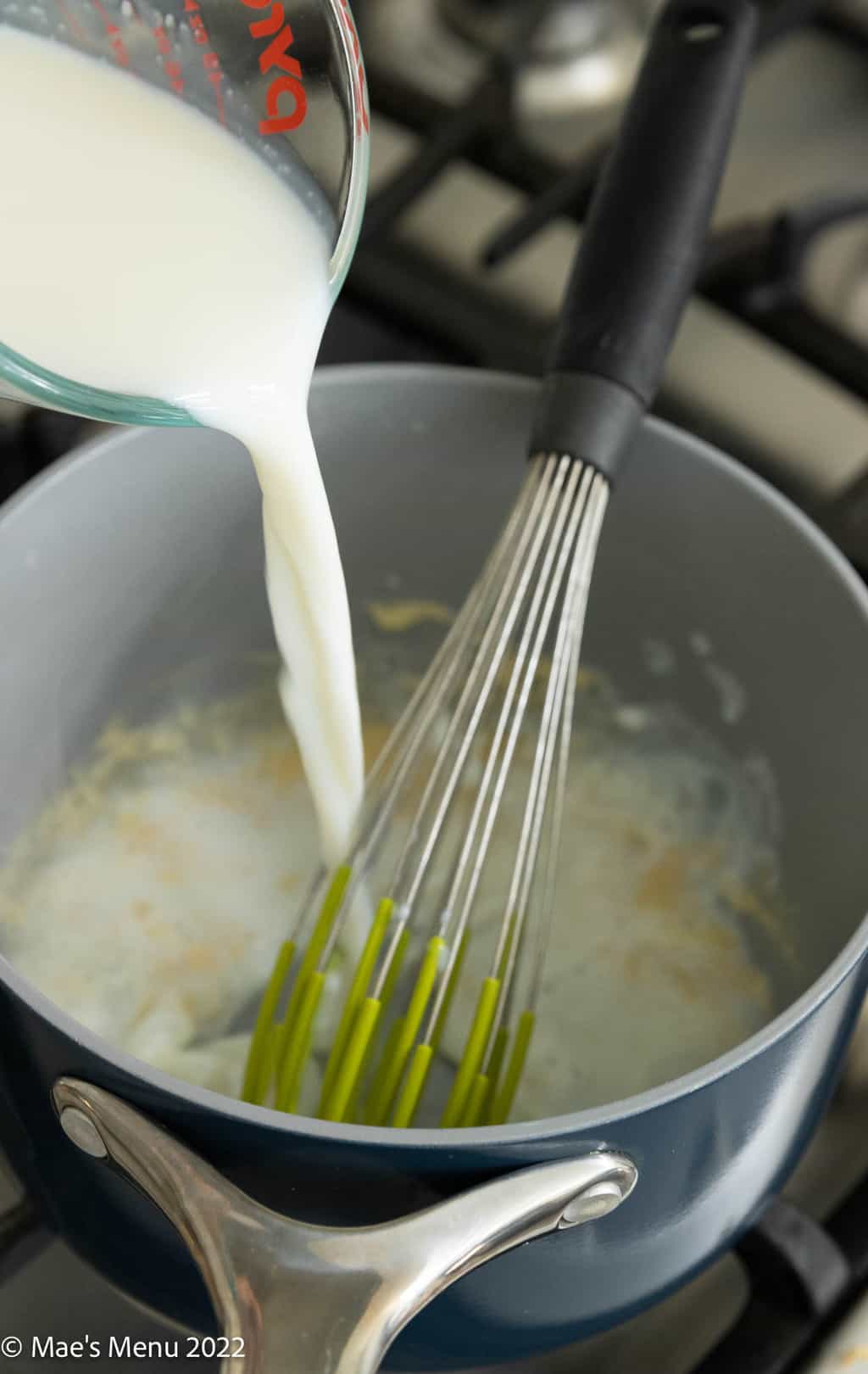 Pouring milk into the saucepan with the roux and whisk.