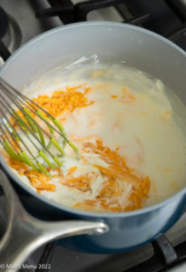 Whisking the roux sauce, cheese, and Greek yogurt together.