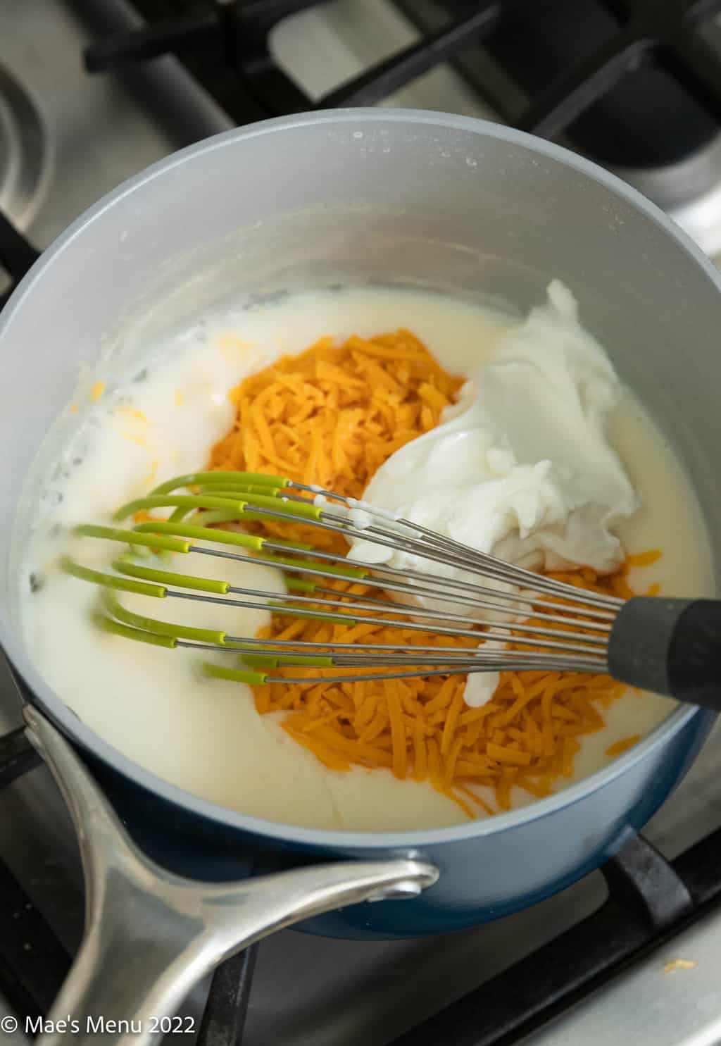 The saucepan with cheddar cheese, Greek yogurt, and a whisk.
