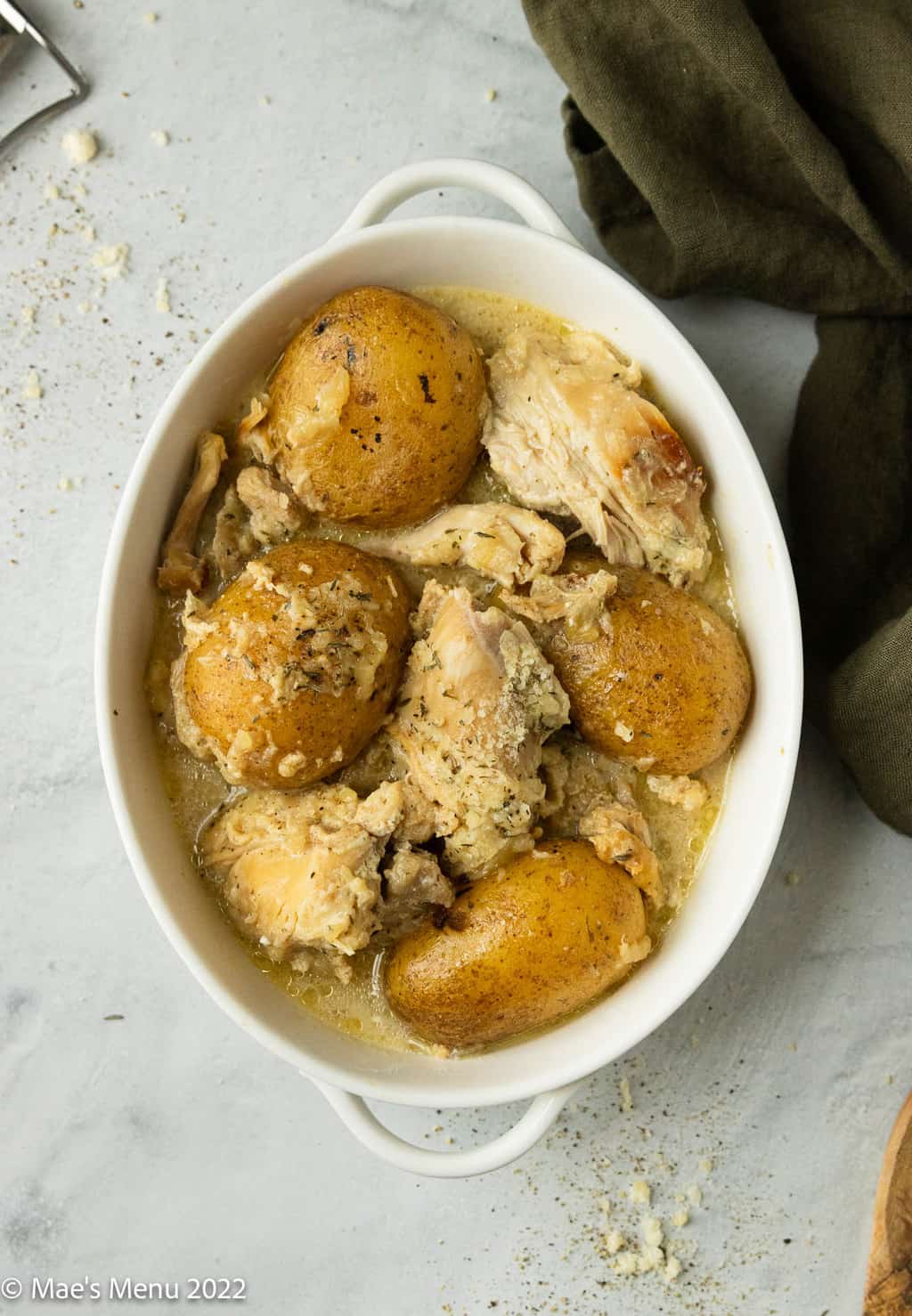An overhead shot of a white bowl of chicken and potatoes in a creamy sauce.