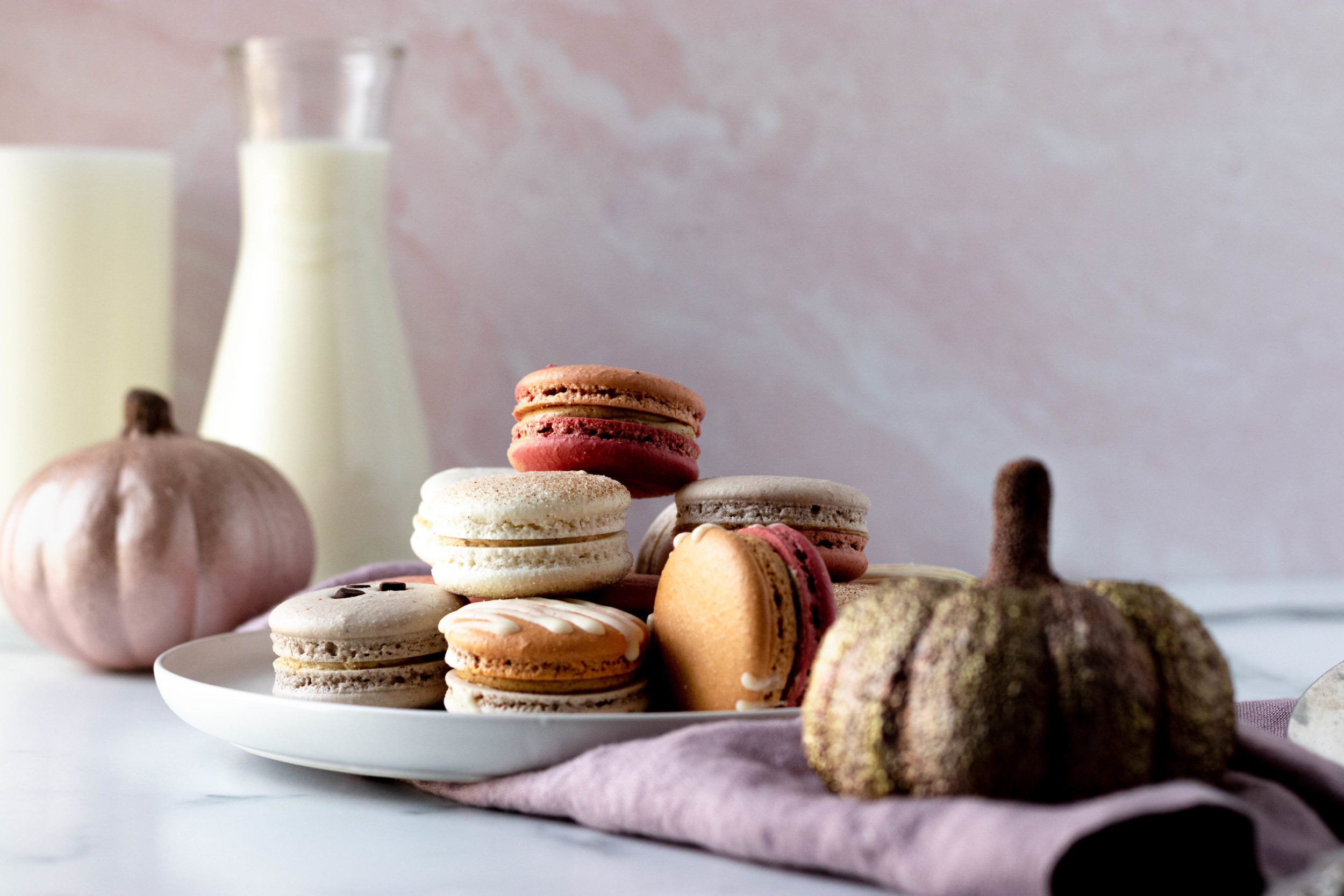 Poeme macarons with pumpkins, milk, and candles on a counter.