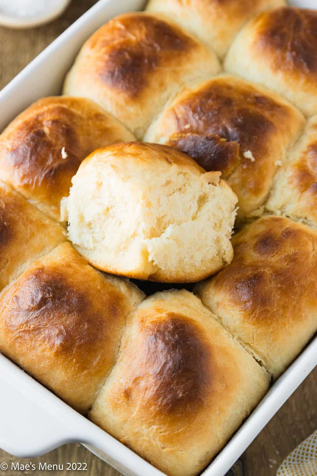 A sweet yeast roll on top of a pan of rolls.