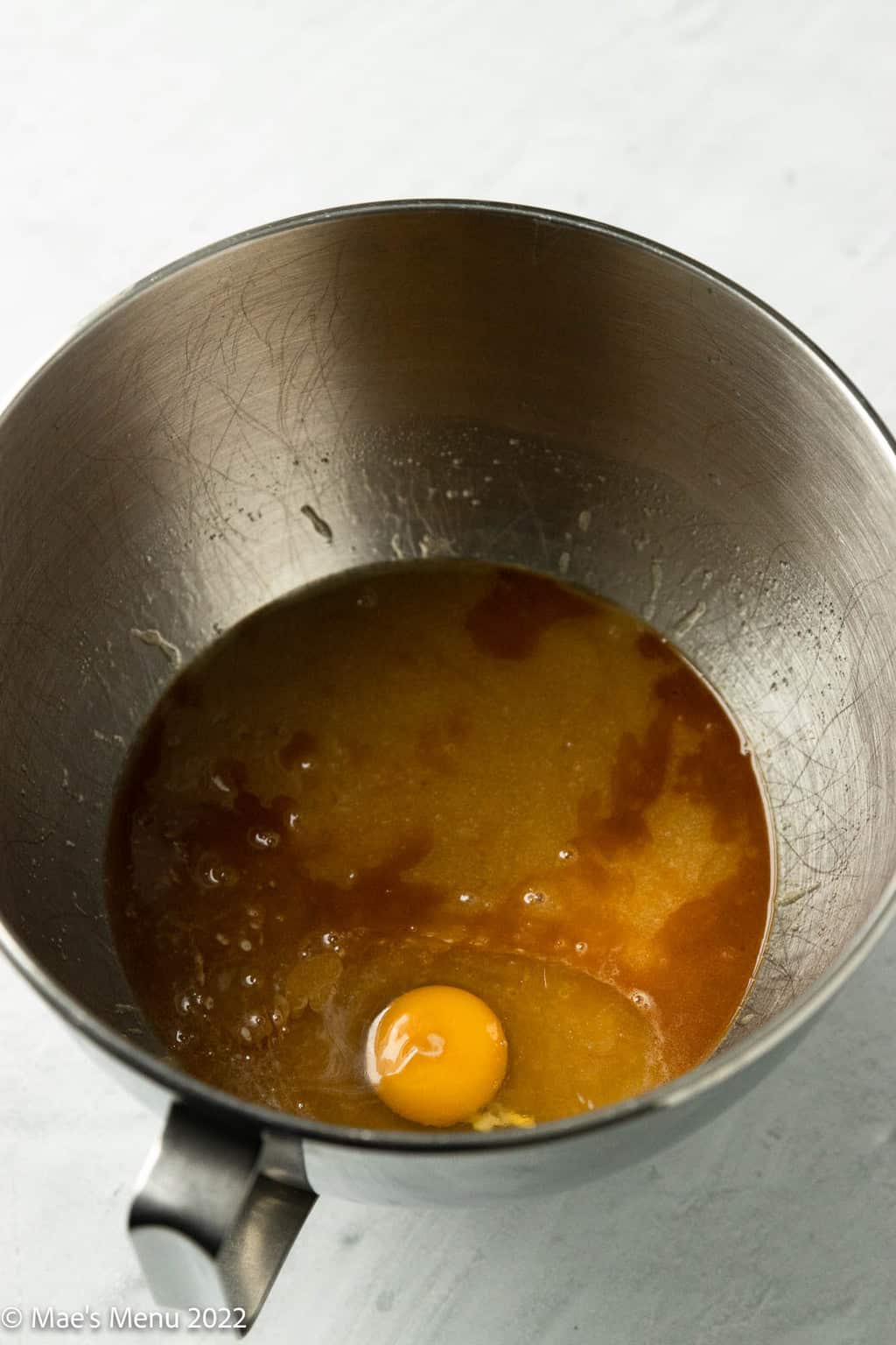 A bowl of melted butter and sugar mixture with an egg and vanilla extract.