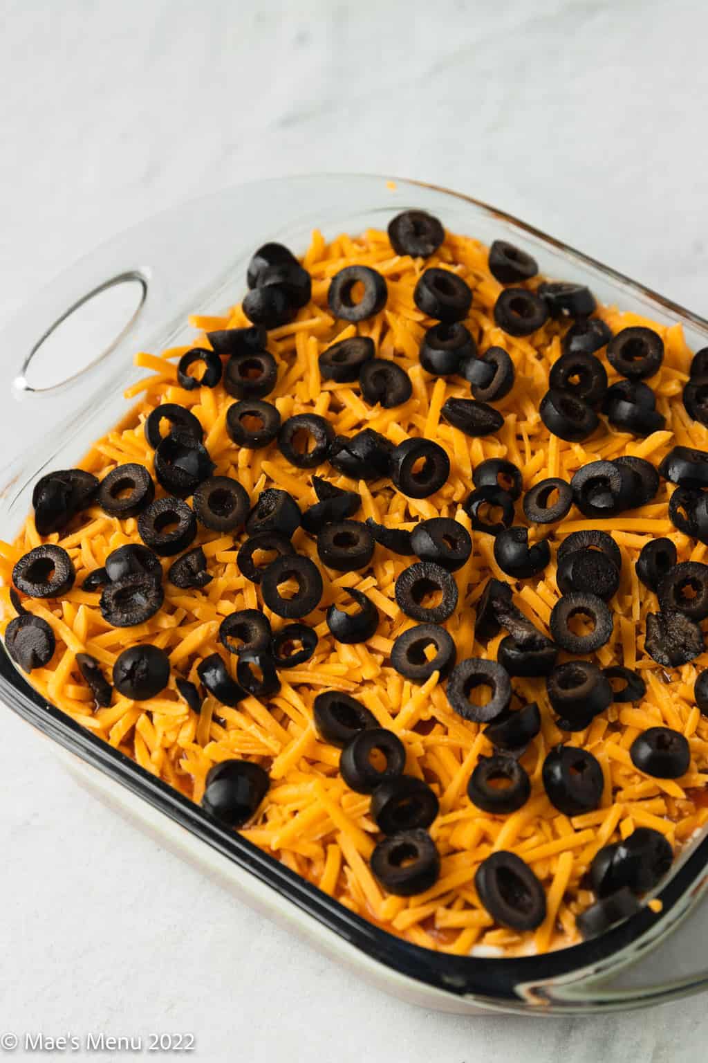 A clear dish of Mexican bean dip on a concrete counter.